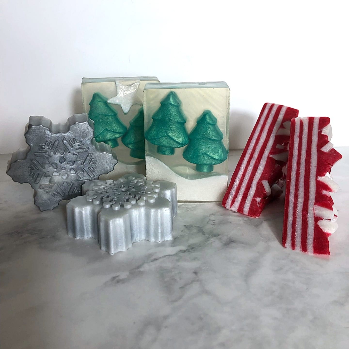 Three festive bars of soaps. One is a grey snowflake, one features a christmas tree design and the last one is red and white striped to replicated a candy cane.