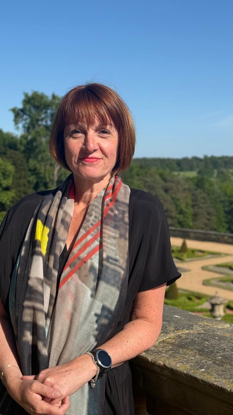 A smiling person with chin-length brown hair, wearing an animal print shirt dress