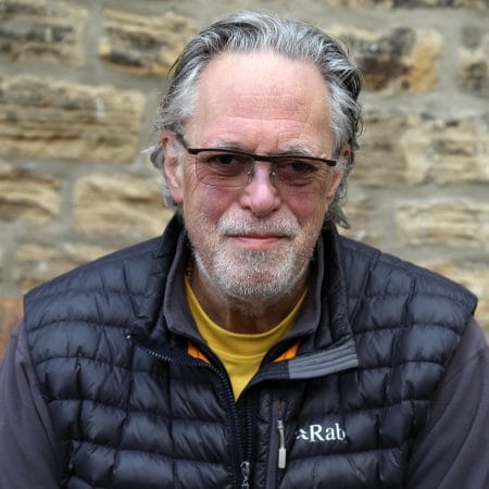 David Lascelles, Earl of Harewood. David has grey hair and a beard, and is wearing a padded black jacket and tinted sunglasses.