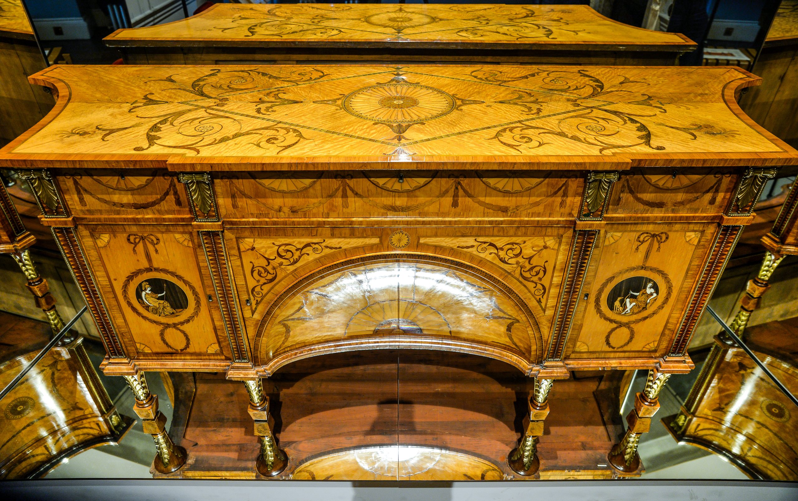 A large wooden dressing cabinet decorated with intricate marquetry patterns on a honey-coloured ground. Two marquetry roundels decorate the left and right sides, depicting the Roman godesses Diana and Minerva.