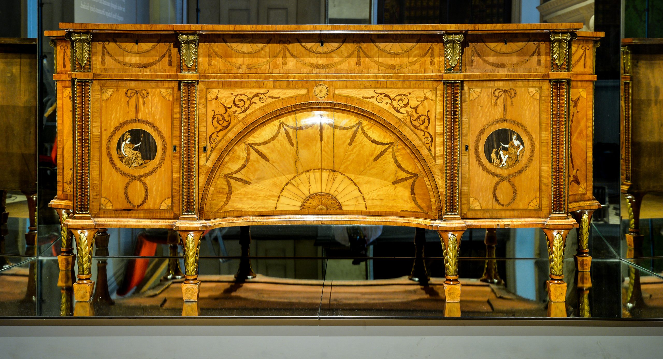 A large wooden dressing cabinet decorated with intricate marquetry patterns on a honey-coloured ground. Two marquetry roundels decorate the left and right sides, depicting the Roman godesses Diana and Minerva.