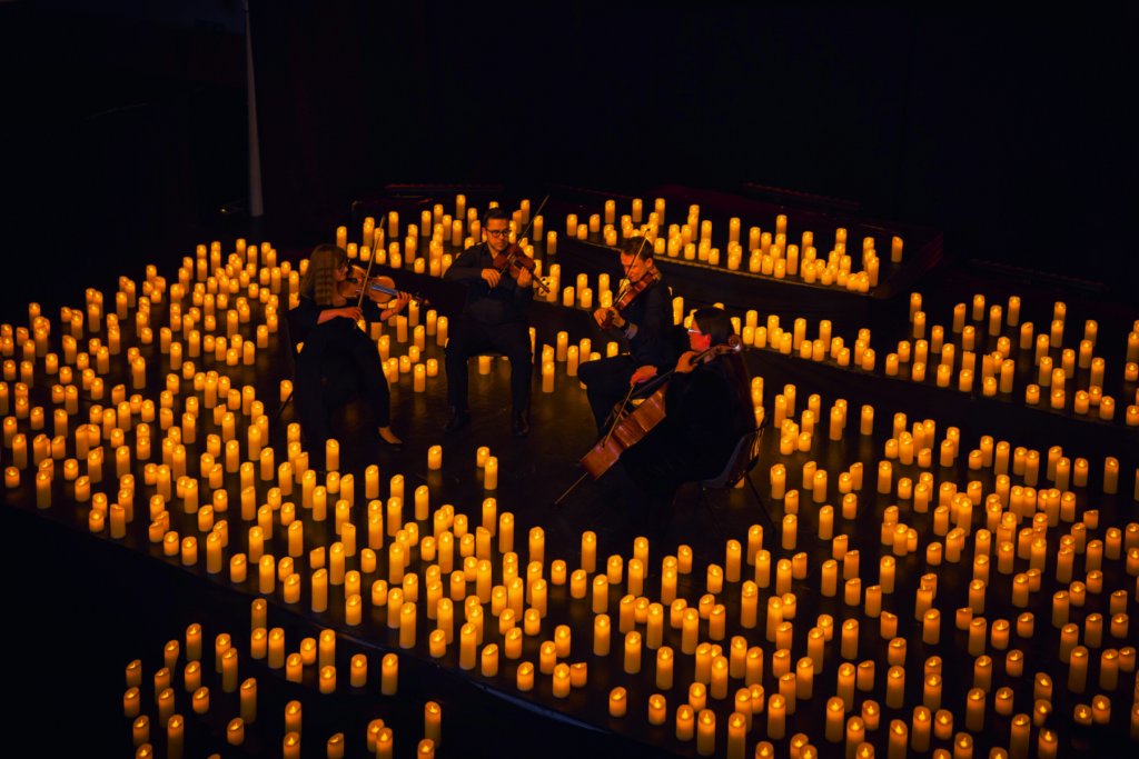 A group of quartet performers seated in a circle, illuminated by the warm glow of surrounding candles