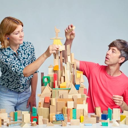 A man and woman collaboratively constructing a tower using colourful wooden blocks on a table.