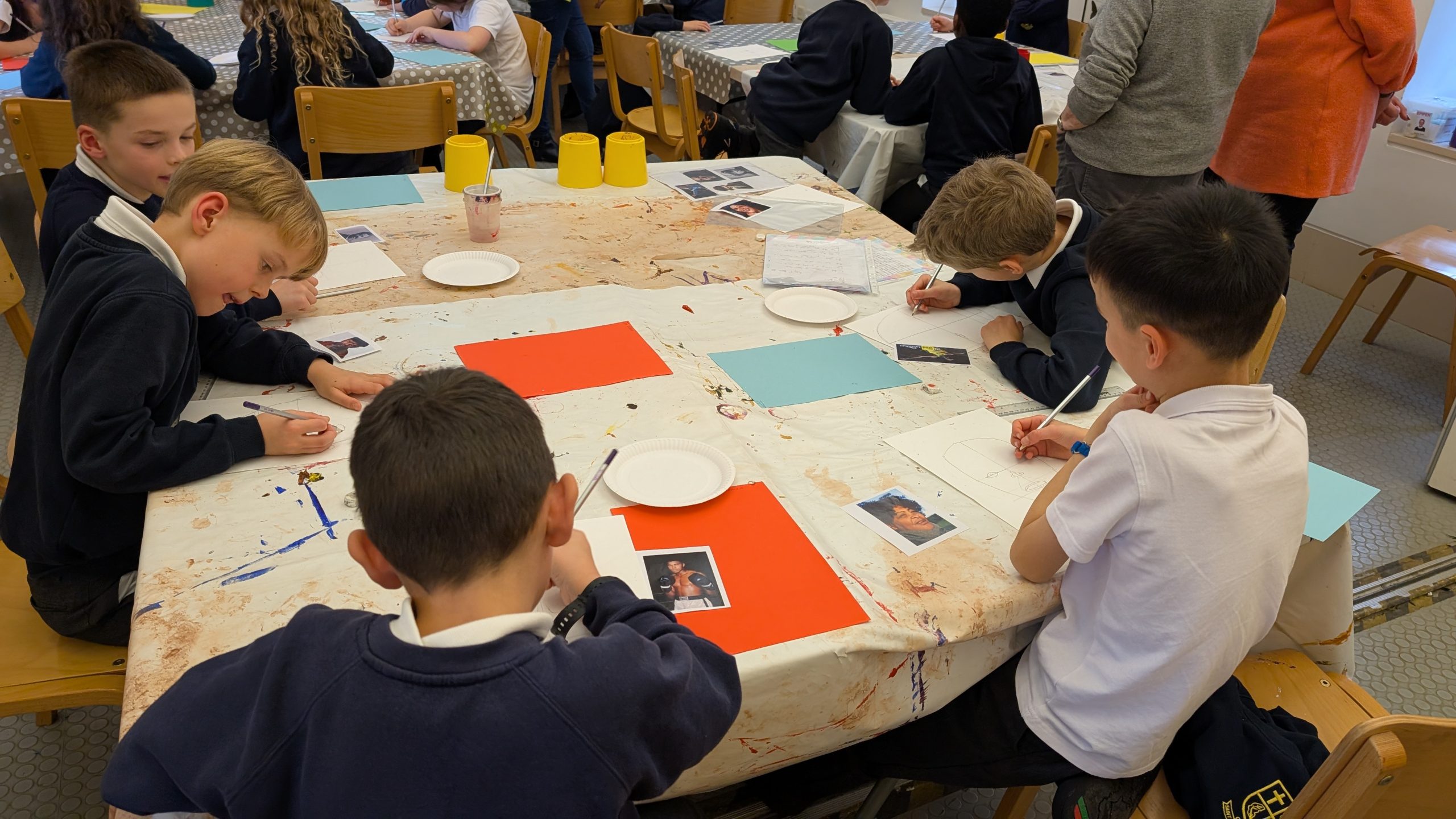 A group of children gathered around a table, engaged in creative activities with paper and pens.