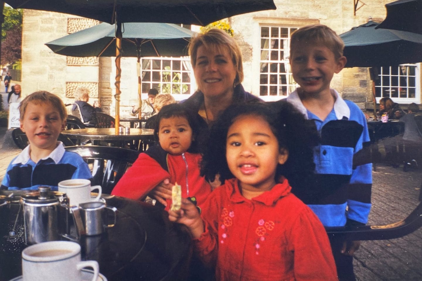 Family photo of an adult with 3 young children and a baby, sat around an outdoor table at Harewood Courtyard Cafe.