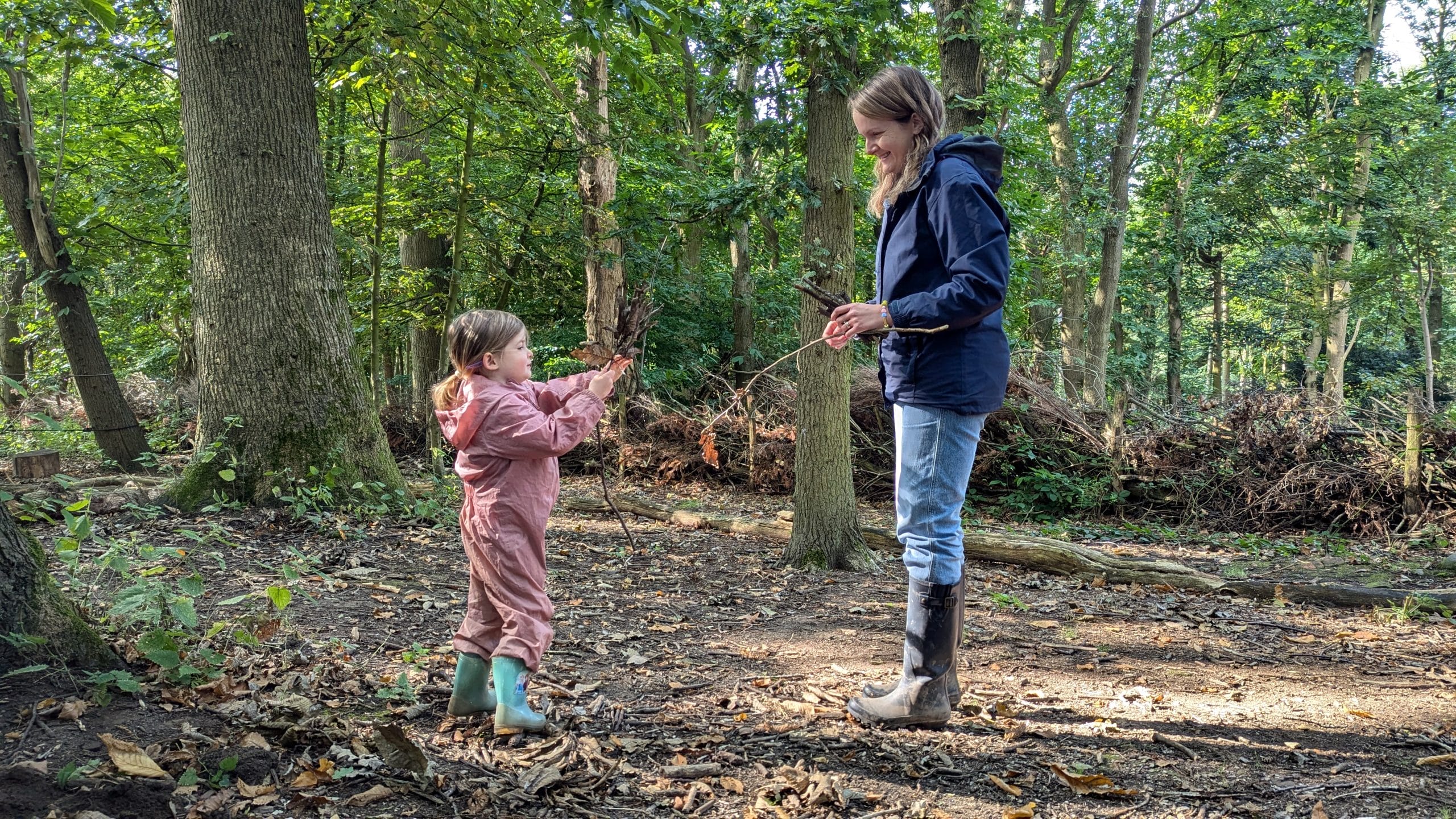 A woman and a young girl walking together through a serene forest, surrounded by trees and natural beauty.