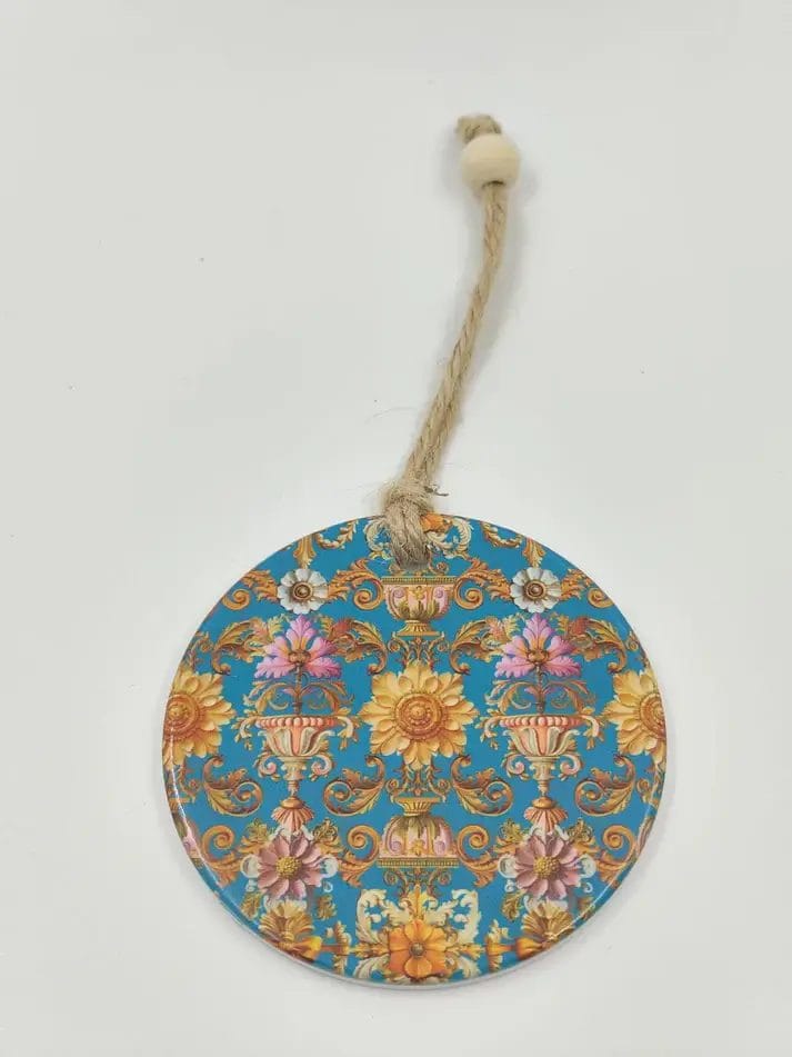 A round, glossy hanging ornament with an ornate blue background and a detailed, symmetrical pattern of golden vases and colourful pink and yellow flowers, featuring a natural string hanger with a wooden bead.