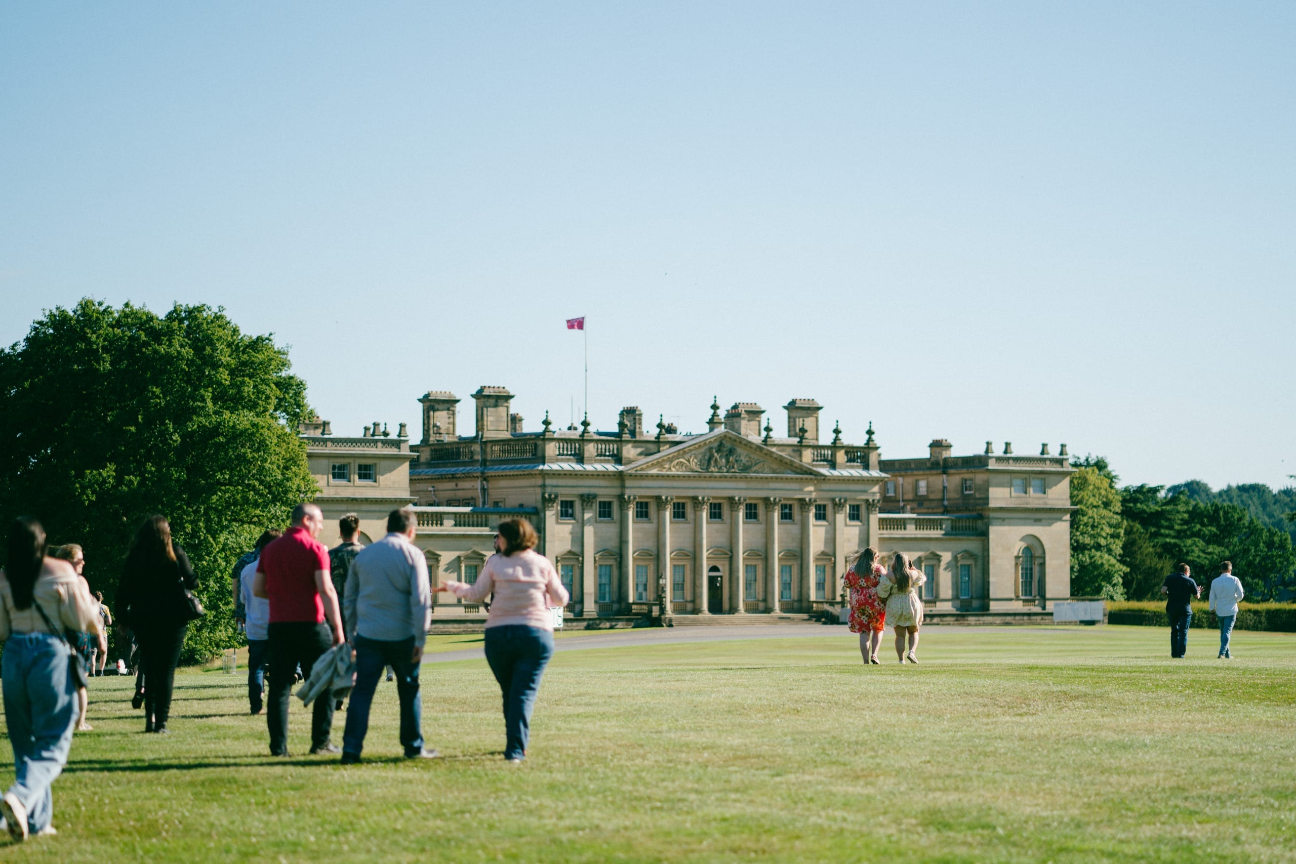 A group of people walk across the North Front lawn outside Harewood House on a late summers evening.