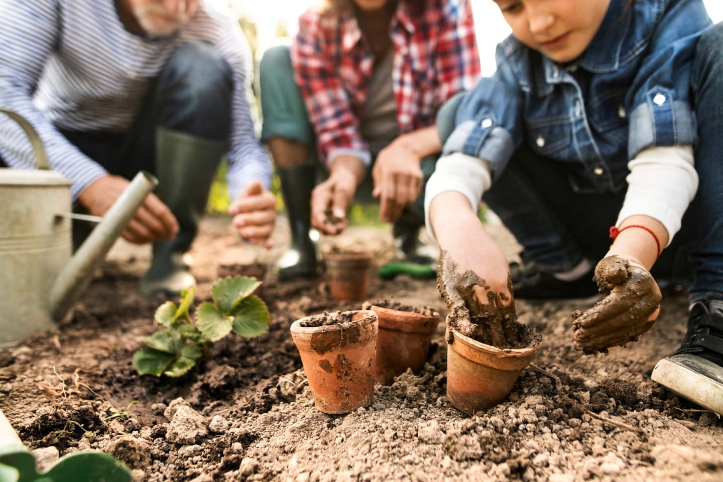 A young boy and two adults crouched planting seeds in plant pots.